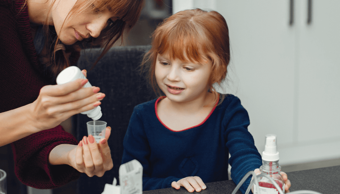 A woman assists a young girl to take medicine without spitting it out