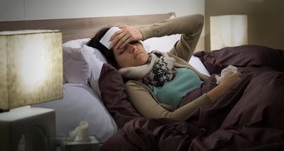 A woman lying in bed with a pillow covering her head in cloth due to flu